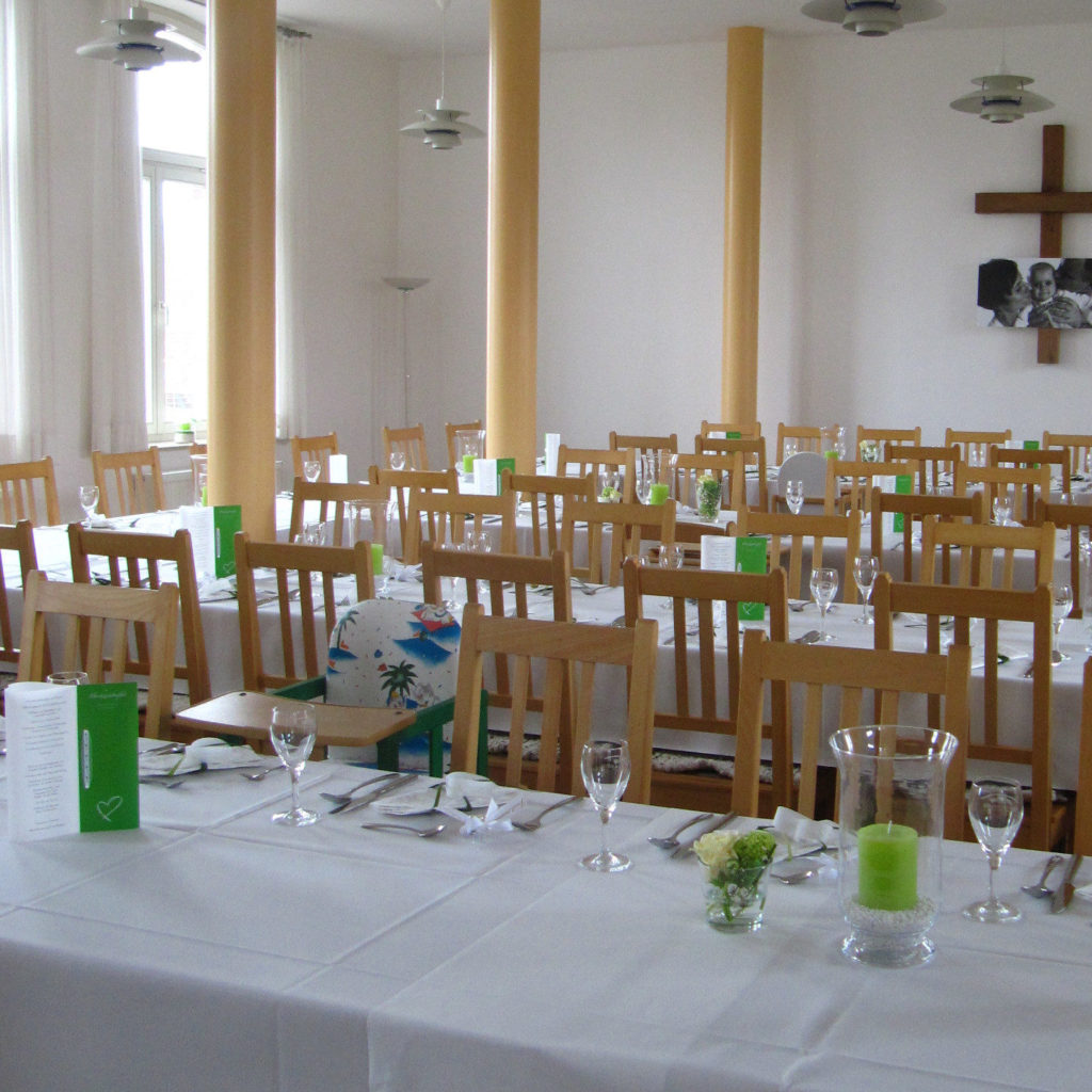 Gedeckte Tischreihen in Saal mit Kreuz